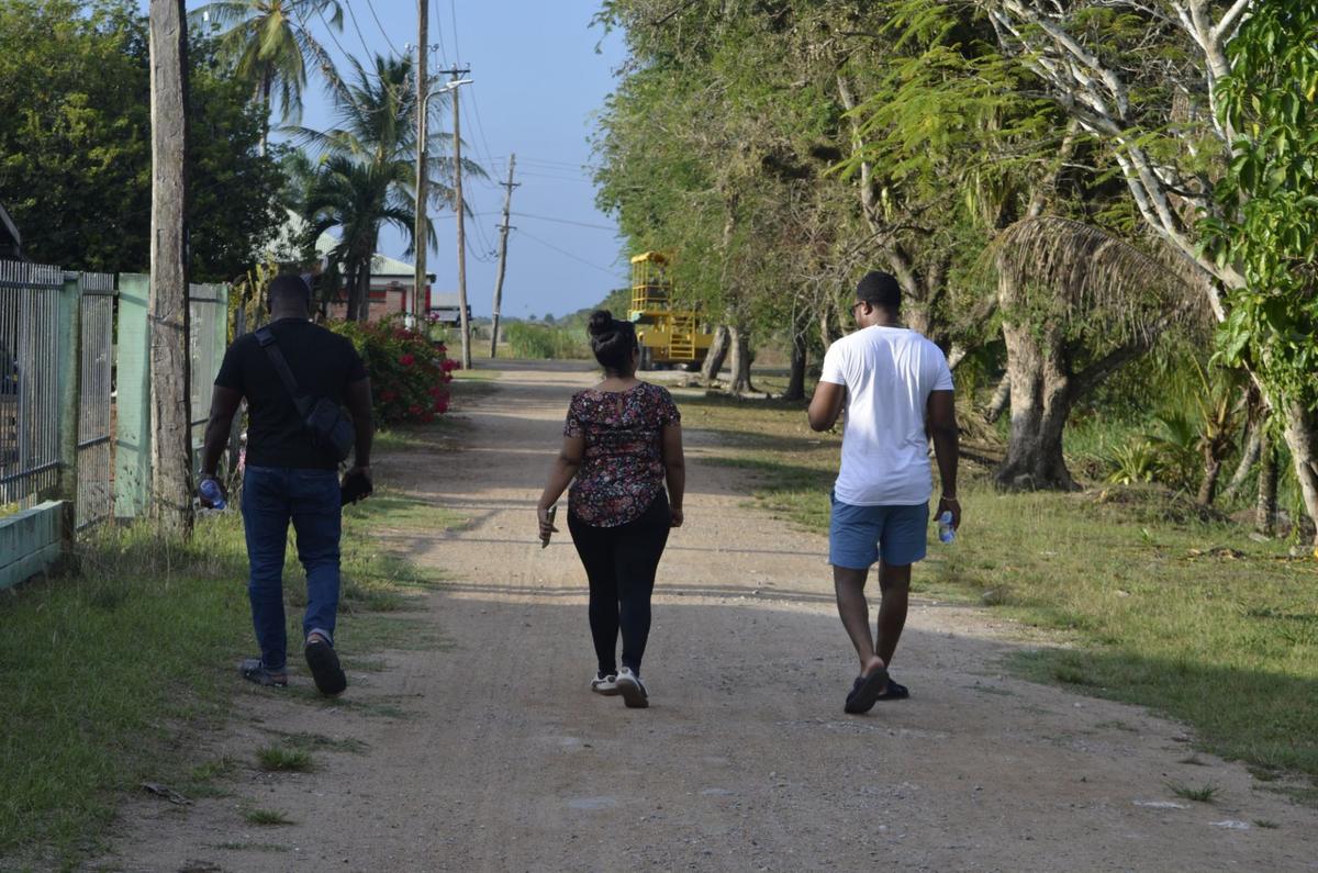 Three guests walking away from the camera along a sandy lane lined with trees and palms
